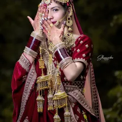A shy, beautiful pose from the bride. The focus is on her stunning kalire and the intricate details of her wedding attire.