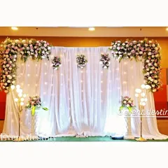 For a clean and sophisticated look, we created this all-white stage with fairy lights embedded in the drapes. The setup is framed by lush floral arrangements on the corners and floor, perfect for an elegant engagement party.