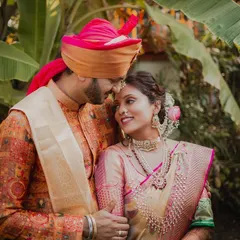 The loving gaze between a Maharashtrian couple, framed by lush banana leaves. The groom's vibrant pheta and the bride's traditional jewelry complete this picture of cultural elegance and affection.