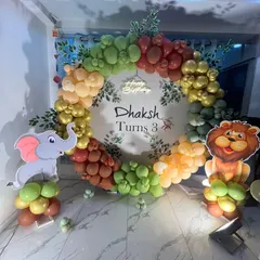 A circular jungle theme backdrop for a third birthday. The balloon wreath is made of various shades of green and orange, with lion and elephant cutouts standing guard.