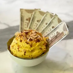 A closer look at the Daulat ki Chaat, adorned with toasted almonds and served with our signature faux currency. It's a playful nod to the dessert's origins as a 'rich man's dish'.