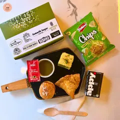 This is a great example of our popular pure veg snack box, starting at just ₹75. It includes a balanced mix of savory items like a samosa and dhokla, a mini bun, chips, a drink, and condiments. It's the perfect light meal for hi-teas and corporate breaks.