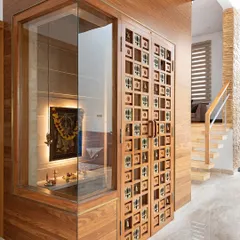 The pooja room in the Cube House is enclosed in glass, making it a visual feature of the home. The custom-designed wooden doors with small bells and motifs add a unique, handcrafted touch to the modern design.