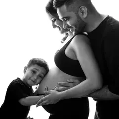 A classic black and white maternity portrait showing the whole family embracing the baby bump. The older brother-to-be gives a gentle hug, creating a timeless and emotional image.