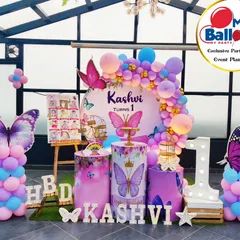 A stunning butterfly-themed first birthday on a rooftop. This outdoor setup features a beautiful balloon arch, large butterfly props, and a 'ONE' marquee table, all complemented by hanging greenery for an enchanting garden feel.