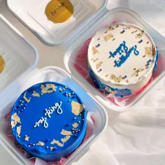 A pair of coordinated bento cakes. One is a solid royal blue with gold leaf, and the other is a white cake with blue script and matching gold accents, creating a beautiful set.