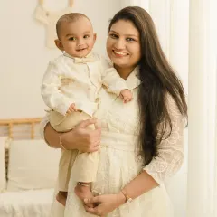 A beautiful mother and son portrait. The mother holds her smiling baby boy, both dressed in light colors that complement the bright and airy feel of the studio.