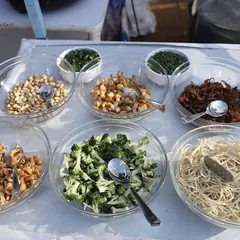 Freshness is key to great food. This image shows the variety of fresh toppings and ingredients we provide for our live stations, including noodles, broccoli, nuts, and fried onions for Khowsuey or pasta.
