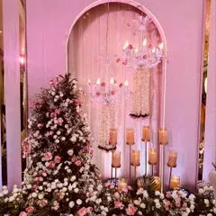 A close-up of a decor element for a pastel-themed event. This setup combines a floral arrangement with a delicate chandelier and candle stands, creating a romantic and intricate corner.