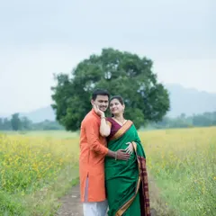 An expecting couple stands together in a vast field of yellow wildflowers, dressed in beautiful traditional Indian attire. This outdoor maternity portrait captures a serene and classic pose, highlighting their bond against a natural, picturesque backdrop.