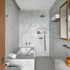 The bathroom in the Worli Duplex is clad in white Carrara marble, creating a serene and monolithic space. The minimal palette is complemented by fluted wood accents, ensuring visual continuity with the rest of the home.