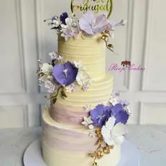 A true labor of love, this three-tier engagement cake is adorned with 45 meticulously handcrafted and fully edible purple and white flowers. Each petal was shaped by hand to create a stunning floral masterpiece.
