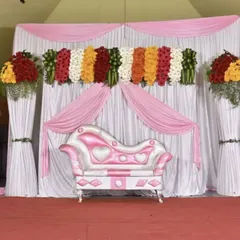 This reception stage uses soft pink and white drapes to create a dreamy atmosphere. The look is completed with large, lush floral arrangements on pedestals, framing the seating area perfectly.