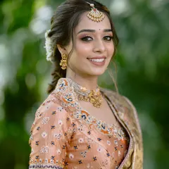 A close-up of the bride's happy face. The makeup is soft and natural, with a focus on enhancing her features and complementing the traditional gold jewellery.