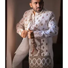 A stylish portrait of the groom getting into his wedding sherwani. The intricate embroidery on his outfit, featuring a doli design, is a unique and personal detail.