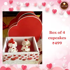 A box of four delicate cupcakes topped with whipped cream and tiny hearts, presented in a beautiful heart-themed box for Valentine's Day.