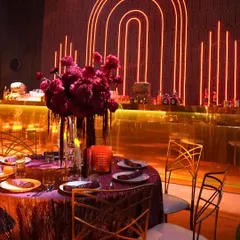 The guest tablescape, featuring rich magenta linens, gold chairs, and deep red floral centerpieces, all set against a neon-lit Art Deco backdrop.