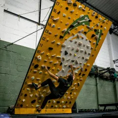 A climber executes a powerful move on the MoonBoard. The steep angle and small holds are designed to build serious finger strength and core stability for advanced rock climbing.