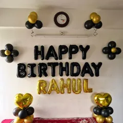 A simple and classic birthday wall decoration for Rahul. The setup uses black and gold balloons, with foil letters and heart-shaped balloon pillars.