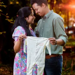 Holding up a tiny baby onesie is a classic and heartwarming way to announce your excitement. This photo captures that joyful anticipation during a golden hour outdoor session.