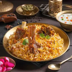 Mutton Biryani styled in a traditional brass plate. The shot highlights the tender, fall-off-the-bone meat and fragrant rice, making it a centerpiece for The Mughal House's menu.