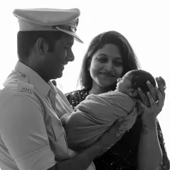 A beautiful black and white family portrait with their newborn. The father, in his police uniform, looks lovingly at his child, held securely by the mother. This image is a timeless testament to a new family's love and pride.