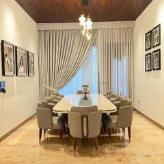A full view of the magnificent 10-seater dining table. The combination of the wooden ceiling, statement chandelier, and plush, comfortable chairs makes this room feel both opulent and welcoming.