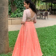 A closer look at the back of this peach Sangeet lehenga. The V-neck blouse is fully embroidered, and the flowing organza skirt is detailed with small, scattered floral motifs for a romantic feel.