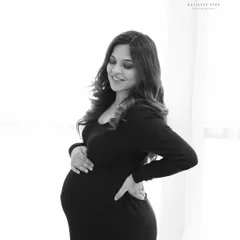 A close-up black and white shot, capturing a gentle smile and the loving way a mother holds her bump. It's a quiet, beautiful moment.