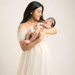 A mother gazes lovingly at her sleeping baby, her expression a mix of awe and adoration. The soft studio light enhances the gentle, peaceful mood.