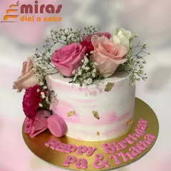 A beautiful cake with a pink marble buttercream finish, adorned with fresh roses, baby's breath, and delicate gold leaf. A single pink macaron adds a touch of modern elegance.