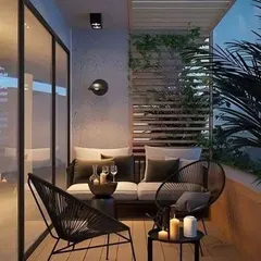 This balcony achieves a sophisticated evening look with modern black wireframe chairs and subtle, warm lighting. The wooden deck and slatted privacy screen add texture and warmth, creating an intimate and stylish setting.