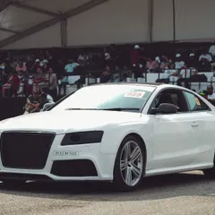 A pristine white Audi S5 waits at the starting line, engine ready to roar. The packed grandstands in the background are a testament to the massive crowd we draw for every race.