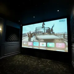 The large screen comes to life in this dark, moody theater. The classic wall paneling and sconce lighting add a touch of old-world Hollywood glamour to the modern tech setup.