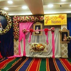 A beautiful naming ceremony setup featuring a floral-decorated swing cradle as the centerpiece. The design includes a large floral ring with the baby's photo and a "Guess My Name" sign for a playful touch.