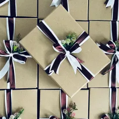 An overhead shot of our meticulously wrapped gift boxes. The combination of rich burgundy and crisp white ribbons with a small floral accent creates a look of pure elegance.
