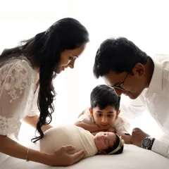The whole family admiring their newest member. A beautiful moment with mom, dad, and big brother looking down at the sleeping newborn.
