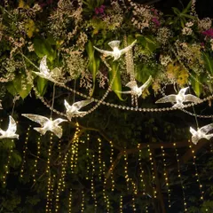 A whimsical decor detail featuring illuminated crystal birds and delicate fairy lights hanging from a floral arrangement, creating a magical, starry-night effect.