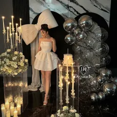 A glamorous birthday girl poses within her stunning party setup. The decor features a dramatic white bow, elegant candelabras, and a backdrop of silver disco balls, creating a high-fashion, celebratory atmosphere.