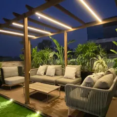 A perfect example of a modern terrace designed for real life. This setup features a custom wooden pergola with integrated LED lighting, comfortable all-weather furniture, and a backdrop of tropical plants, creating an ideal space for hosting or relaxing.