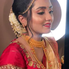 A side profile showcasing the complete Muhurtham look. You can see the elegant hair bun adorned with flowers, the glow on her skin, and how the gold jewellery perfectly complements the makeup.