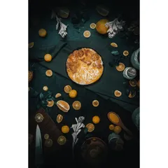 This elaborate flat lay captures a lemon dessert surrounded by fresh and dried citrus slices. The dark, desaturated color palette creates a sophisticated and artistic image, perfect for editorial features.