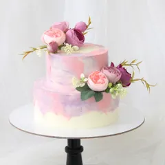 A lovely two-tiered cake with a pink, purple, and mauve watercolor effect. The design is beautifully balanced with arrangements of fresh peonies on each tier.