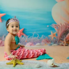 This little mermaid is interacting with a starfish prop, adding a playful element to the scene. These details help keep babies engaged and happy during the shoot.