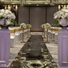 A stunning pathway for a Christian wedding. The aisle is lined with grand white floral arrangements and features a reflective, water-like surface that creates a dramatic and elegant entrance.