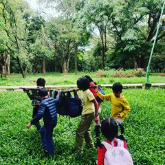 Teamwork and play combine as children use a large branch to carry their backpacks through Cubbon Park, turning a simple walk into a fun, collaborative challenge.
