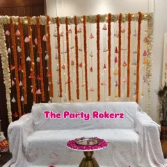 A traditional backdrop for a home kirtan. The decor consists of a seating area with a backdrop of marigold and bell strings, illuminated with fairy lights.