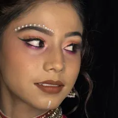 A creative airbrush makeup look featuring decorative pearl bindis and sharp, graphic eyeliner. This demonstrates how airbrush techniques can be used for both a flawless base and artistic details.