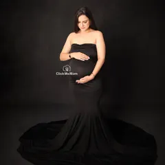 A classic and elegant portrait focusing on the beauty of the baby bump. This form-fitting black gown drapes beautifully, creating a timeless silhouette against a simple dark backdrop for a powerful, minimalist maternity photo.