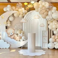 A dreamy "Twinkle Twinkle Little Star" first birthday theme. The decor includes a large crescent moon prop with a sleeping teddy bear, cloud cutouts, and a soft, neutral-toned balloon garland.